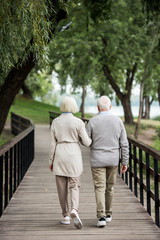 Fototapeta na wymiar senior couple walking across wooden bridge in park