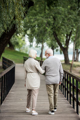 Fototapeta premium senior couple talking while walking across wooden bridge in park