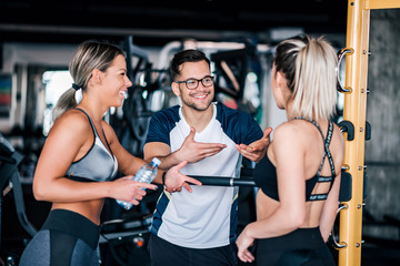 Two beautiful fit sports women talking with a handsome guy at the gym.