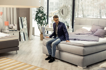 Good-appealing beaming man resting on new bed in furniture store