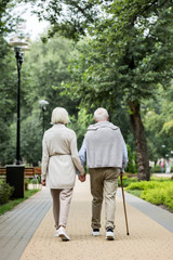 back view of stylish senior couple enjoying walking in park