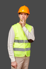 The man the builder in a helmet and a vest applied a forefinger to lips