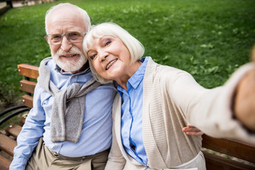 selective focus of happy senior couple sitting on wooden bench in park