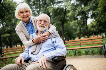 smiling senior woman with husband in wheelchair in park