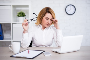 stressed or tired mature female doctor sitting in modern office