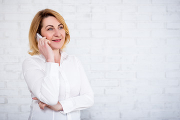 portrait of mature business woman talking by phone over white wall
