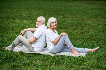 smiling senior couple relaxing on yoga mats in park