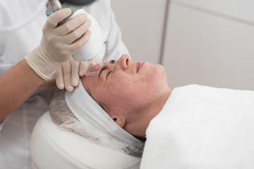 Fototapeta na wymiar Face beauty treatment. Close-up of woman getting facial laser polishing and rejuvenation face procedure, cosmetologist using hardware apparatus