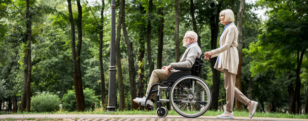 senior woman with husband in wheelchair walking in park