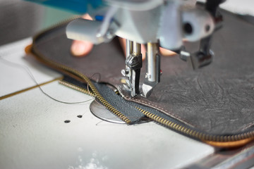 Designer stitching a fragment of a leather bag on the sewing machine