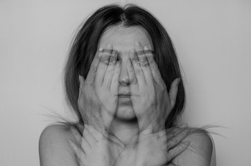 Young charming girl blurred by multiple exposure covers her eyes and shoulders with her hands isolated on a light background