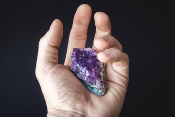 druse of natural untreated violet crystals of amethyst on a piece of rock lies on the palm of your hand