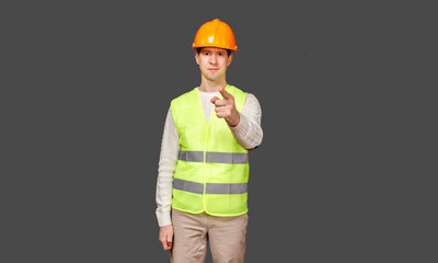 The man the builder in a helmet and a vest points a finger in the camera