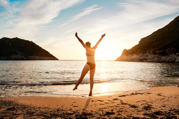 Fototapeta na wymiar A woman jumping for joy on the seashore at sunset