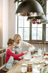 Mother and daughter wearing striped apron and cooking on wooden kitchen table