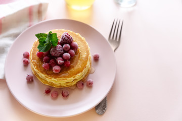 Stack of pancakes with frozen raspberry, red currant and honey on pink background. Selective focus