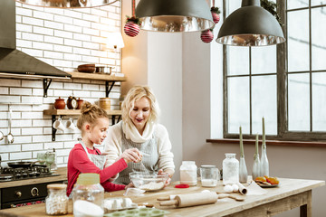 Pleasant short-haired mother spending time with daughter on furnished kitchen