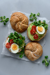 Bagel sandwiches with cream cheese, avocado, tomatoes, egg and greens on gray wooden background. Selective focus. Healthy eating or vegetarian food concept