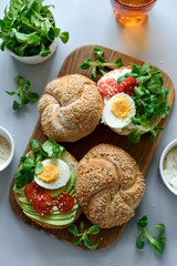 Bagel sandwiches with cream cheese, avocado, tomatoes, egg and greens on gray wooden background. Selective focus. Healthy eating or vegetarian food concept
