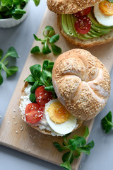 Bagel sandwiches with cream cheese, avocado, tomatoes, egg and greens on gray wooden background. Selective focus. Healthy eating or vegetarian food concept