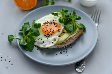 Toast (sandwich) with cream cheese, avocado, fried egg and greens on gray wooden background. Selective focus. Healthy eating or vegetarian food concept