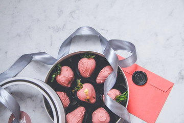 Chocolate-covered strawberries in a gift box with a transparent lid and a gray ribbon and envelope...