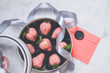 Chocolate-covered strawberries in a gift box with a transparent lid and a gray ribbon and envelope...