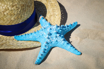 Summer straw hat and blue starfish on the sand