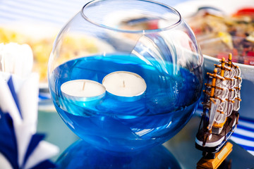 Bright blue water with candles in the glass vase and wooden toy ship. Sea time theme on the party's candy bar