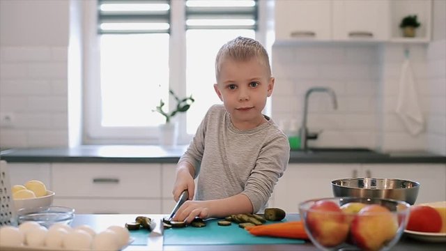 Little beautiful caucasian boy with big blue eyes cooking in the bright kitchen.