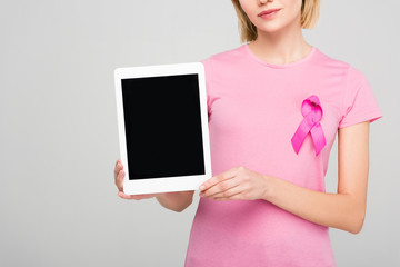 cropped view of  girl in pink t-shirt with breast cancer awareness ribbon holding tablet with blank screen, isolated on grey