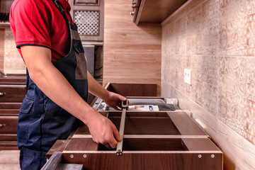 A young worker is assembling modern wooden kitchen furniture.