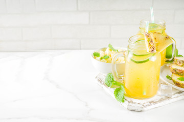 Cold pineapple mojito cocktail with ice, lime and mint, rustic wooden background copy space