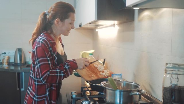 woman mom cooking in the kitchen concept. cooks soup in a pan and pours onions into the pan makes toasting. girl mother in the kitchen indoors lifestyle preparing food concept smart home control on a