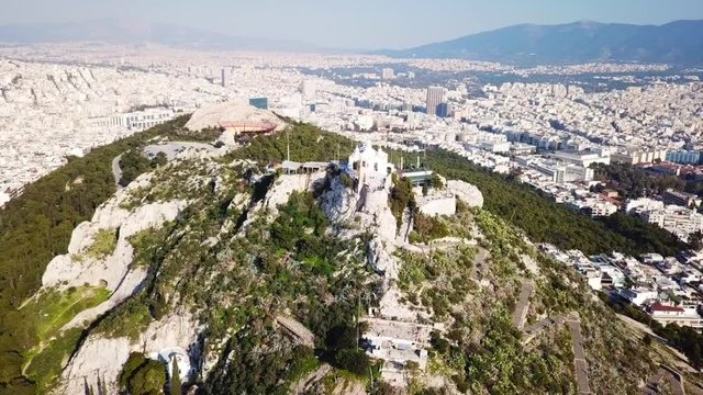 Aerial birds eye view video taken by drone of Lycabettus hill and iconic Saint George chapel on top with beautiful scattered clouds, Athens historic center, Attica, Greece