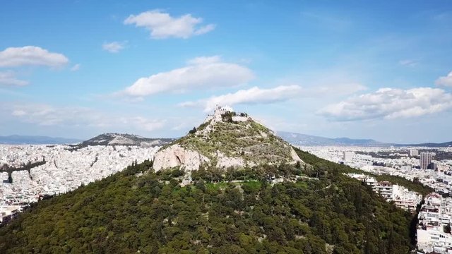 Aerial birds eye view video taken by drone of Lycabettus hill and iconic Saint George chapel on top with beautiful scattered clouds, Athens historic center, Attica, Greece