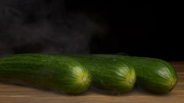 Fresh rotating vegetables cucumbers on a black background in the smoke from which evaporation goes, close-up, slow motion, vegan