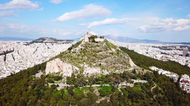 Aerial birds eye view video taken by drone of Lycabettus hill and iconic Saint George chapel on top with beautiful scattered clouds, Athens historic center, Attica, Greece
