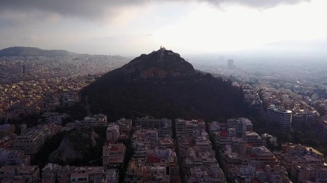 Aerial birds eye view video taken by drone of Lycabettus hill and iconic Saint George chapel on top with beautiful scattered clouds, Athens historic center, Attica, Greece