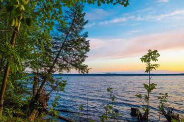 Sunrise, sunset over the river, lake through the green leaves of birch blue sky with clouds.