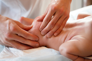 Image from above of newborn baby and masseur hands.
