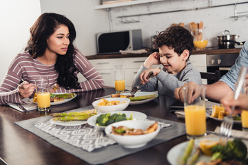 selective focus of latin woman looking at cute son having lunch near father and daughter at home