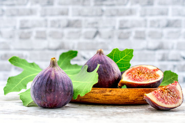 Fresh fruit fig in a wooden bowl on a wooden table. Still life in a rustical style with a brick background. Fruit with green leaf.