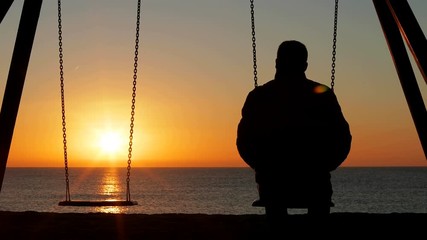 Back view silhouette of a man alone contemplating sunset sitting on a swing on the beach - Powered by Adobe