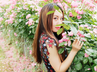 Naklejka premium Beautiful young brunette woman in sexy black dress posing in rose garden. Outdoor fashion portrait of glamour Chinese stylish girl. Emotions, people, beauty and lifestyle concept.