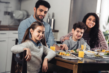 selective focus of happy hispanic kid smiling while looking at camera with latino family on background