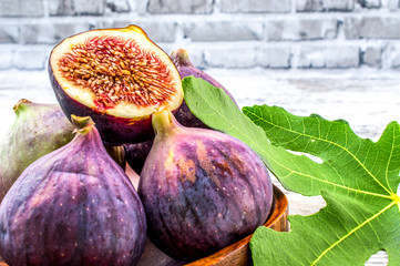 Fresh fruit fig in a wooden bowl on a wooden table. Still life in a rustical style with a brick background. Fruit with green leaf.