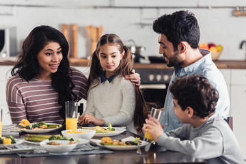 attractive latin mother hugging daughter while looking at son near husband at home
