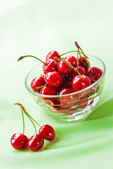Juicy ripe sweet cherries in glass bowl on gently green cloth background