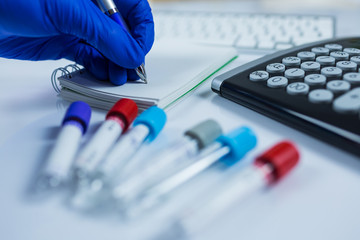Hand wearing blue gloves making notes next to bottles for samples used in hospitals or medicine for blood samples in a laboratory white background